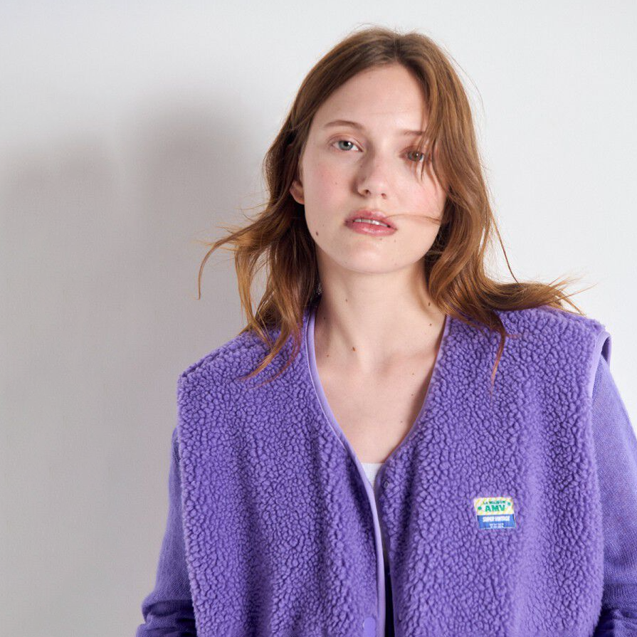 Woman wearing a purple fleece jacket with a brand logo on a plain background
