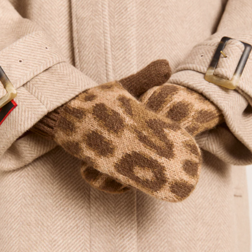 Leopard print gloves held by a person wearing a beige coat with a belt buckle.